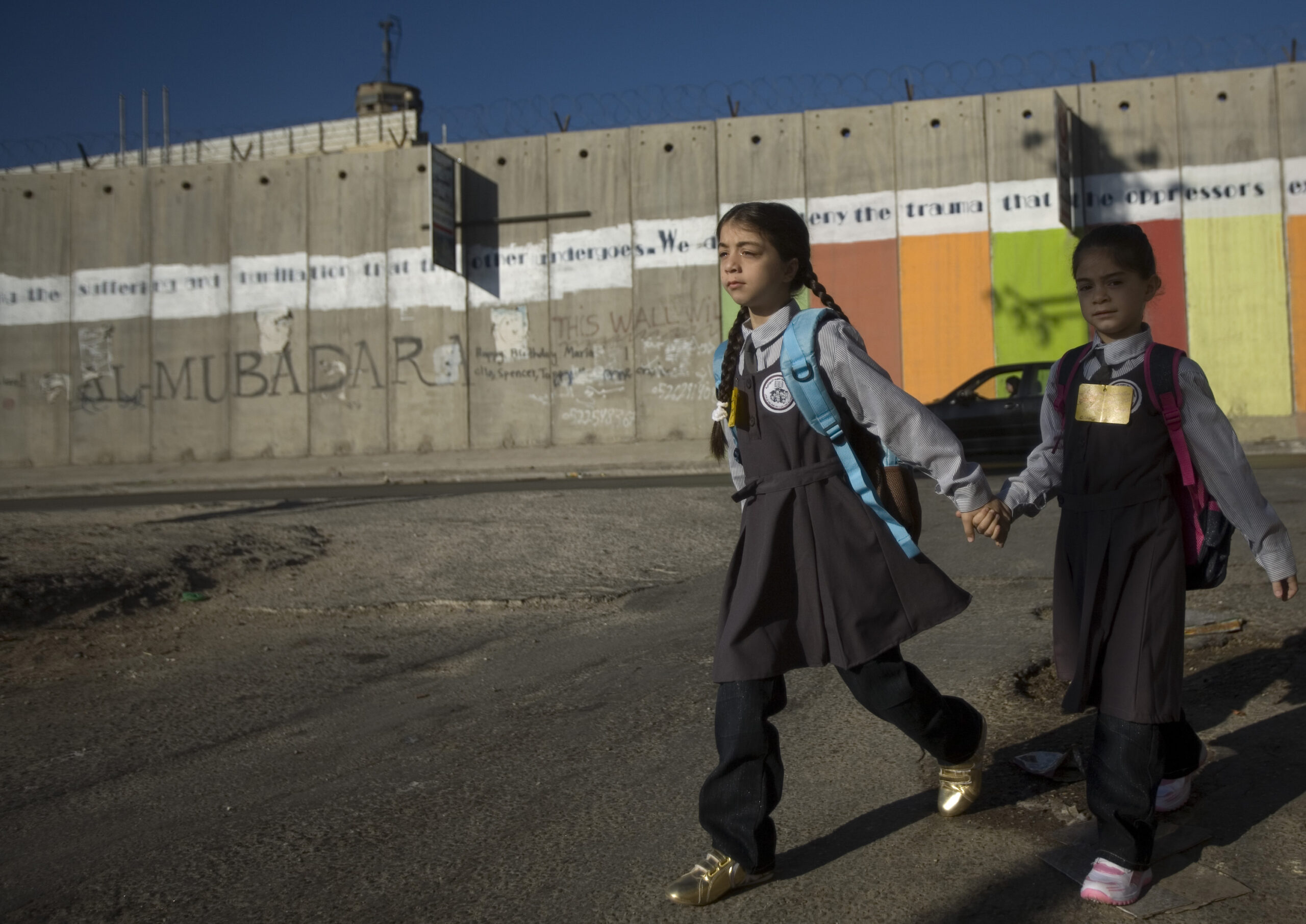Una bambina e un bambino passano davanti al muro di annessione e separazione costruito dal governo israeliano in Cisgiordania mentre vanno a scuola © Per gentile concessione di WeWorld ad Azione contro la Fame.